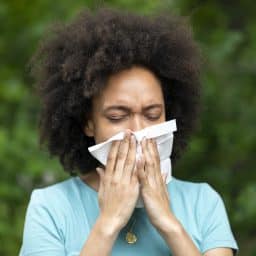 A woman with Sinusitis Problems is Feeling Displeased and Blowing Nose in Napkin During a Walk in City Park During a Summer Day.